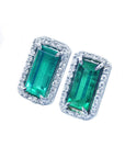 Pair of emerald earrings with halo diamond accents on a white background
