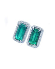 Pair of emerald earrings with halo diamond accents on a white background