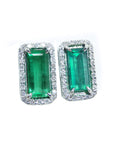 Pair of emerald green gemstone earrings with white gold frames and halo diamond on a white background