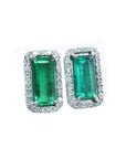 Pair of emerald green gemstone earrings with white gold frames and halo diamond on a white background