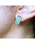 Close-up of an ear wearing a green emerald earring with gold setting.