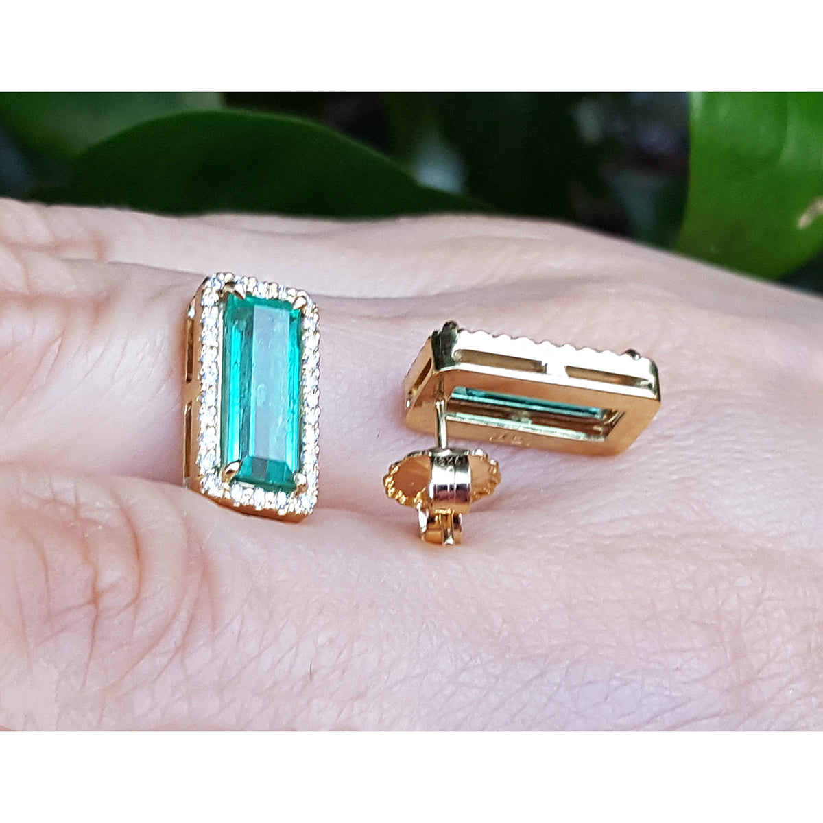 Gold earrings with green emeralds gemstones on a hand