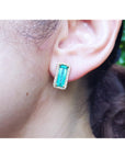 Close-up of an ear wearing a emerald earring with a blurred background