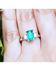 A Colombian emerald engagement ring three stone with side baguette diamonds in white gold on a finger.