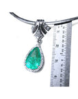 18K white gold enhancer necklace with a pear-shaped emerald and halo diamonds, measured against a ruler.