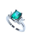 18K white gold three-stone ring with a vibrant emerald and two emerald-cut side diamonds.
