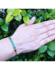 Five emerald-cut Colombian emeralds in a 14K yellow gold bracelet on a woman's wrist.