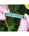 Five emerald-cut Colombian emeralds in a 14K yellow gold bar bracelet, held by fingers.