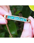 Five emerald-cut Colombian emeralds in a 14K yellow gold bar bracelet, held by fingers.