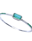 On a tilted position this white gold emerald and diamond bangle bracelet shows its top and partial side profile.