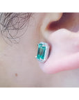Emerald-cut natural emerald stud earring with halo diamonds in 14K white gold, worn on an ear.