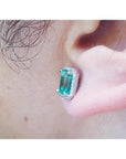 Emerald-cut natural emerald stud earring with halo diamonds in 14K white gold, worn on an ear.