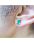 Emerald-cut natural Colombian emerald stud earring with a diamond halo, set in 14K gold on an ear.