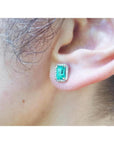 Emerald-cut natural Colombian emerald stud earring with a diamond halo, set in 14K gold on an ear.