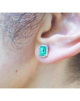 Emerald-cut natural Colombian emerald stud earring with a diamond halo, set in 14K gold on an ear.