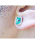 Close-up of an ear wearing a real Colombian emerald stud earring with a diamond halo.