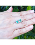A pair of emerald and diamond Colombian emerald stud earrings on a hand with a blurred green background.