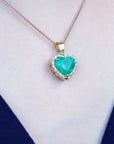 Heart-shaped emerald pendant on a gold chain against a white and blue fabric background.