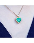 5.04 ct. emerald heart pendant with diamond halo in 18K yellow gold on a woman's neck.