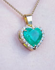Heart-shaped emerald pendant with gold frame and diamonds on a light pink skin background.