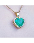 Heart-shaped emerald pendant with gold frame and diamonds on a light pink skin background.