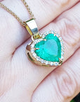 Heart-shaped emerald pendant on a gold chain held on a hand.