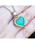 Heart-shaped emerald pendant on a gold chain held on a hand.