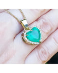 5.04 ct. heart-shaped emerald pendant with diamond halo in 18K yellow gold on a hand.