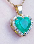 Heart-shaped emerald pendant with gold frame and diamonds on a light pink background.