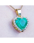 Heart-shaped emerald pendant with gold frame and diamonds on a light pink background.