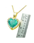 Emerald heart pendant with diamond halo in 18K yellow gold, next to a ruler for scale.