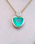 Heart-shaped emerald pendant necklace on a person's neck against a neutral background.