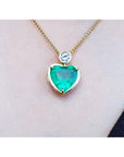 Heart-shaped emerald pendant necklace on a person's neck against a neutral background.