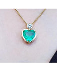 Heart-shaped emerald pendant necklace with a bezel-set diamond on an 18K yellow gold chain.