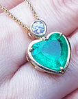 Heart-shaped emerald pendant with gold frame on a person's fingers.