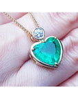 Heart-shaped emerald pendant with gold frame on a person's fingers.