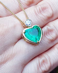 Heart-shaped emerald pendant on a gold chain held on a hand.
