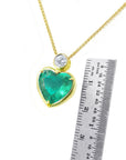 Gold necklace with a heart-shaped emerald pendant next to a ruler for scale on a white background