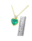 Heart-shaped emerald pendant necklace in 18K yellow gold with a diamond slider bail, shown with a ruler for scale.