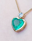 Heart-shaped emerald pendant on a gold chain against a light pink skin background