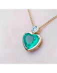 Heart-shaped emerald pendant on a gold chain against a light pink skin background