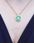 Necklace with a heart-shaped natural emerald gemstone pendant on a person wearing a dark blue top.