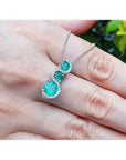 14K white gold emerald journey pendant necklace with three round green emeralds and diamond accents.