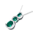 14K white gold journey pendant with three round-cut Colombian emeralds and diamond accents on a chain.