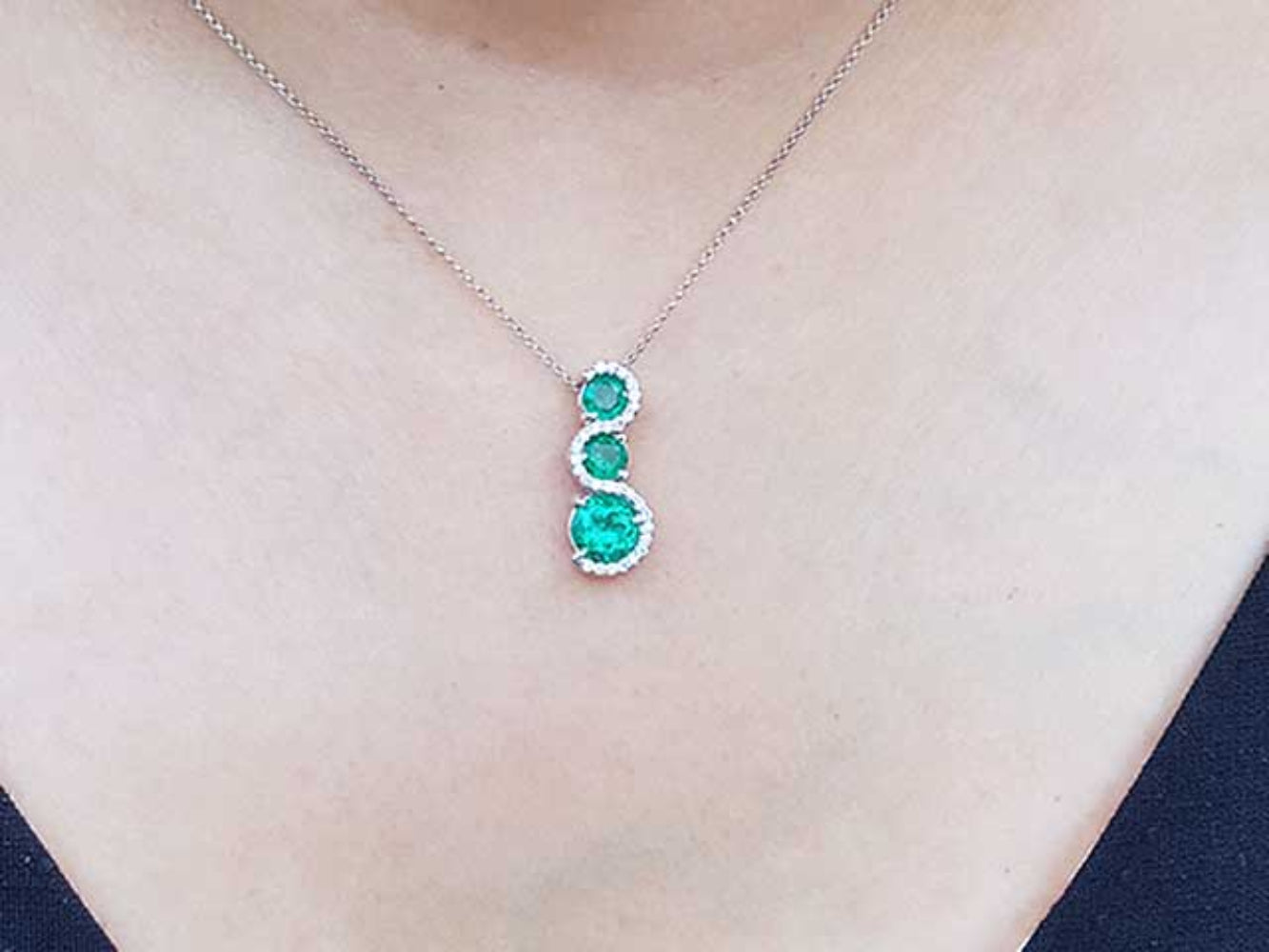 A natural emerald journey necklace on a person's neck against a neutral background.