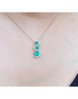 14K white gold journey pendant necklace with three round emeralds and diamond accents.