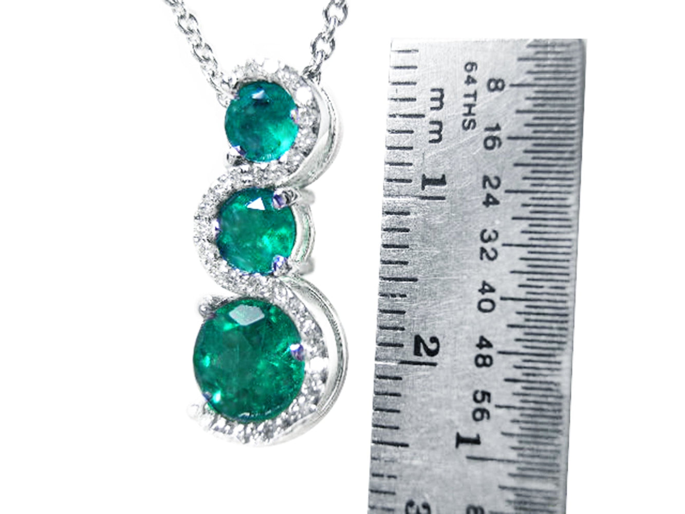 Emerald pendant journey necklace next to a ruler for size reference on a white background