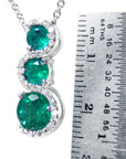Emerald pendant journey necklace next to a ruler for size reference on a white background