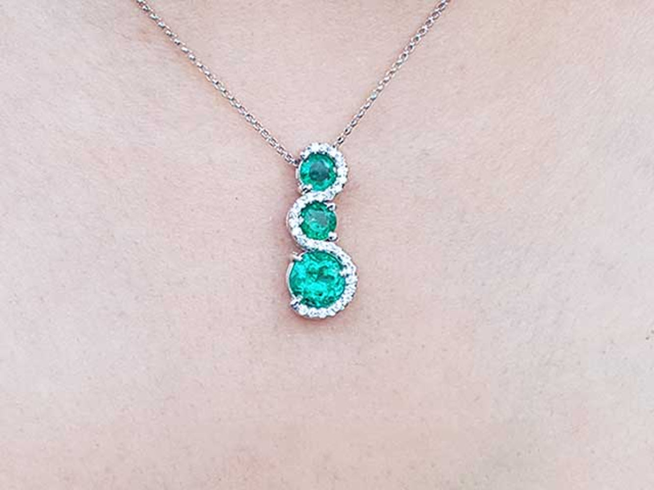 A natural emerald three stone journey pendant necklace on a light skin background.