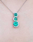 A natural emerald three stone journey pendant necklace on a light skin background.